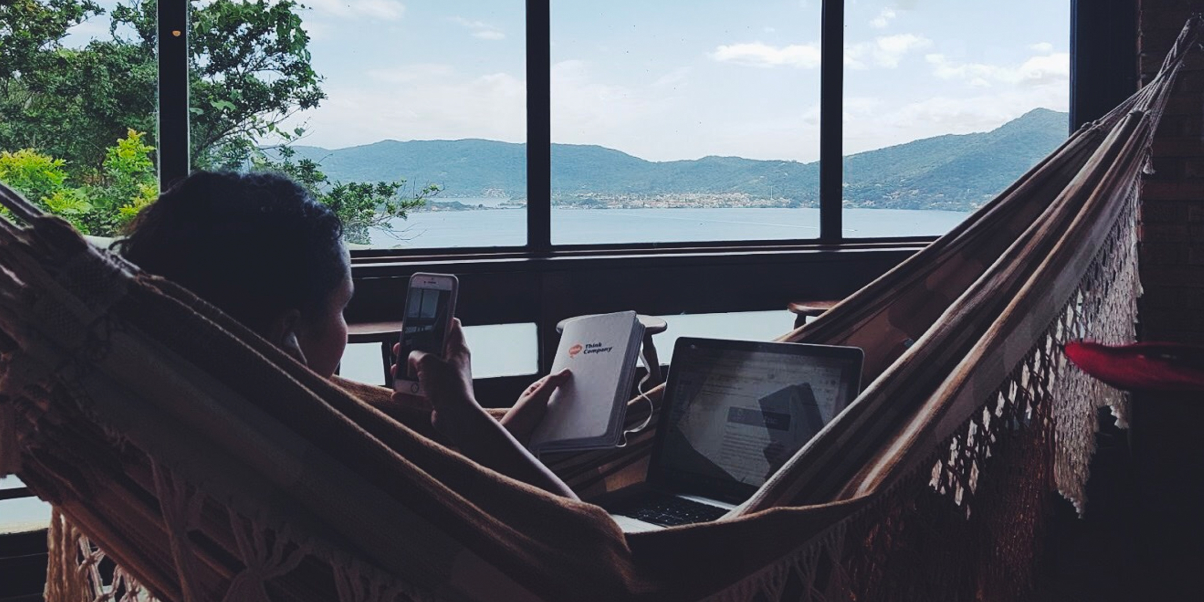 woman in hammock taking photo by water with laptop