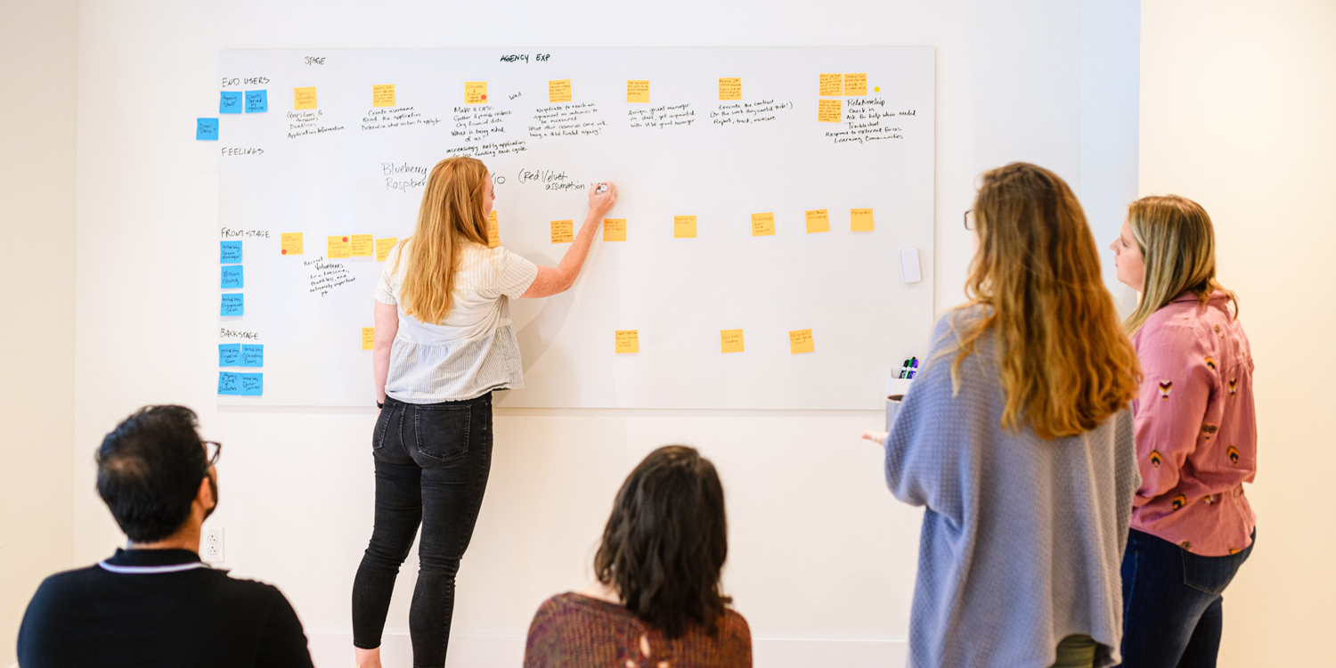 person at a whiteboard with a group of people around watching