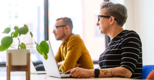 Two people working on their laptops at a conference table