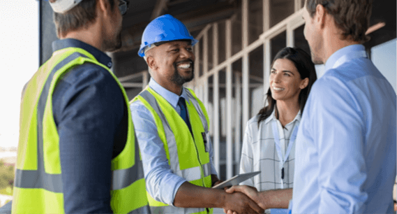 Two construction workers shake hands happily with two business people
