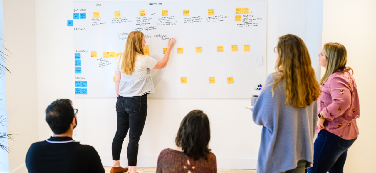 person stands at whiteboard in front of group