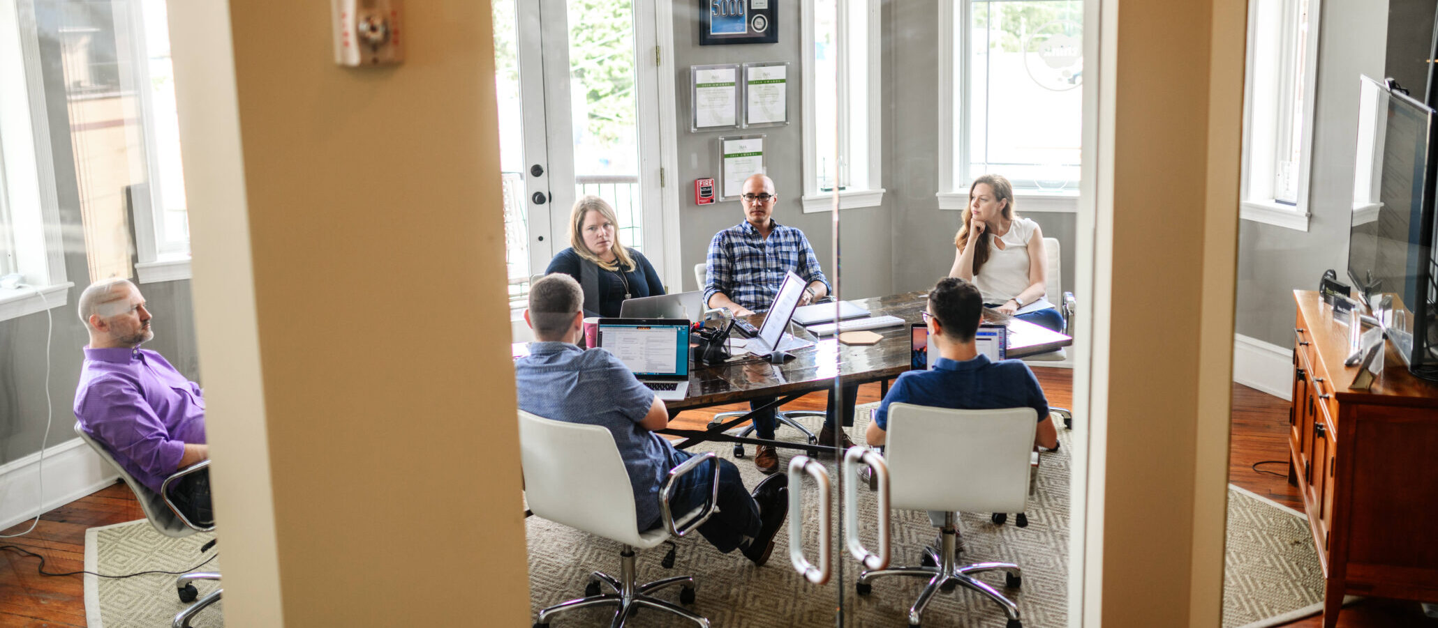 people gathered around a big table in an office with lots of windows