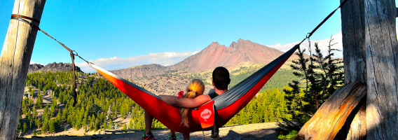 two people laying in a hammock looking at a mountain