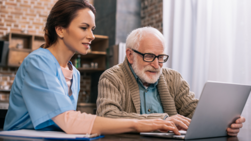 Healthcare provider helping elderly man with glass use a patient portal on a laptop